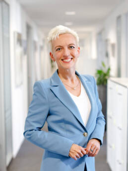 Notariatsassessorin Sylvia Gauß steht mit einem freundlichen Lächeln in einem hellen Büroflur.