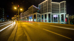 ächtliche Außenaufnahme des beleuchteten Gebäudekomplexes „Das Gerber“ mit Lichtspuren vorbeifahrender Autos auf der Straße.