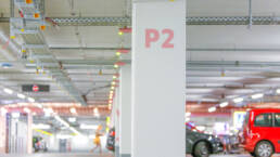 Helles Parkdeck mit einer tragenden Säule, markiert mit „P2“ in Rot, Deckenleitungen und geparkten Fahrzeugen.