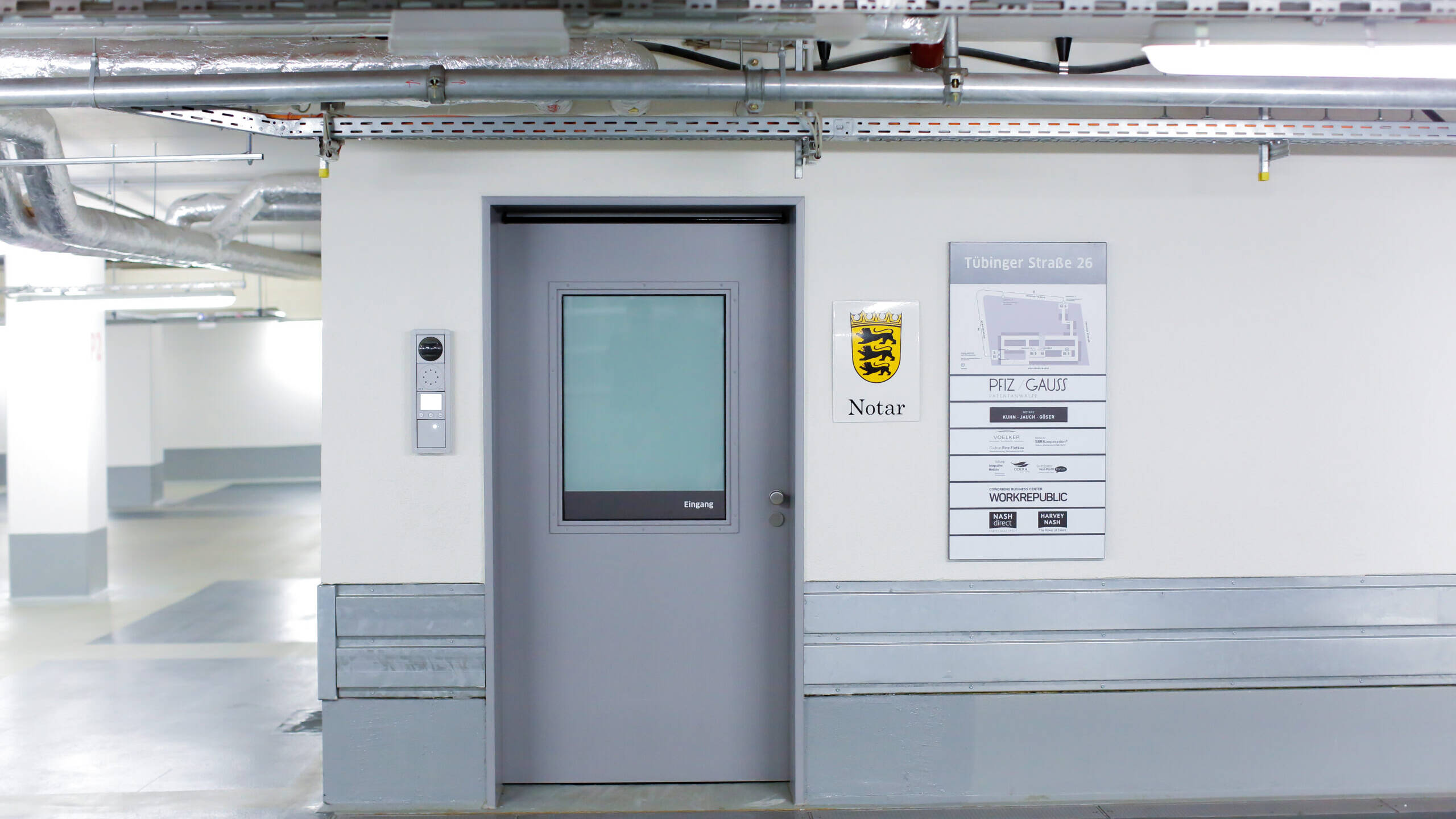 Graue Zugangstür im Parkhaus, daneben ein Notar-Wappenschild und eine Orientierungstafel für „Tübinger Straße 26“.