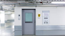 Graue Zugangstür im Parkhaus, daneben ein Notar-Wappenschild und eine Orientierungstafel für „Tübinger Straße 26“.