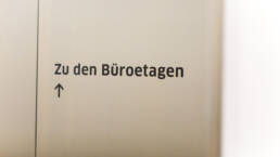 Silbernes Hinweisschild „Zu den Büroetagen“ mit einem Pfeil nach oben.