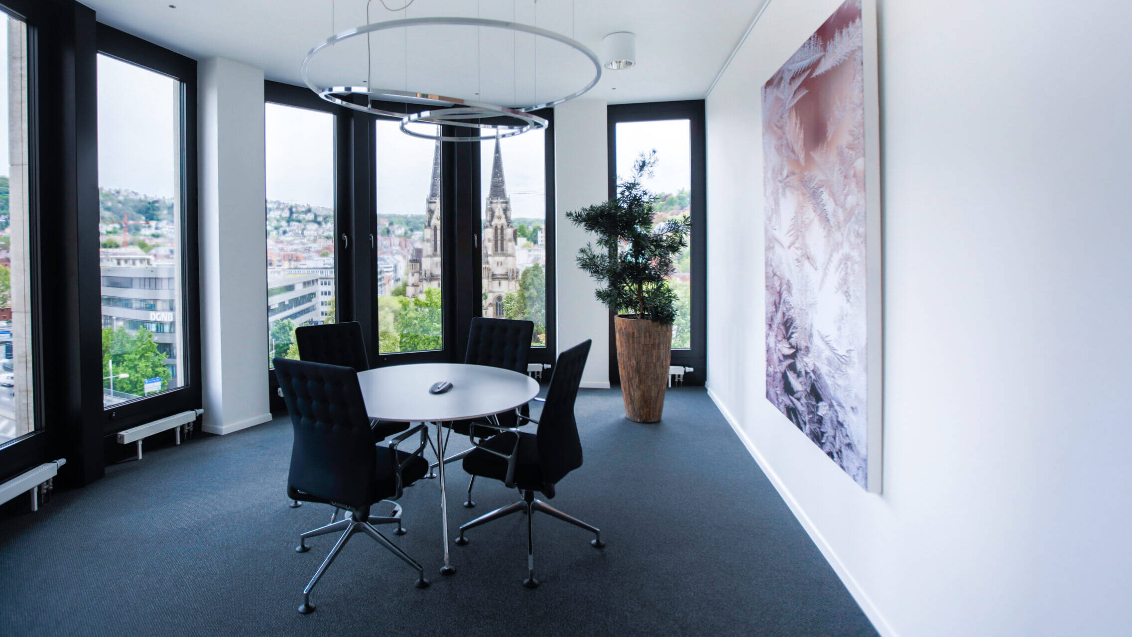 Heller Besprechungsraum mit rundem Tisch, schwarzen Stühlen und Panoramablick über die Stadt und Kirchtürme.